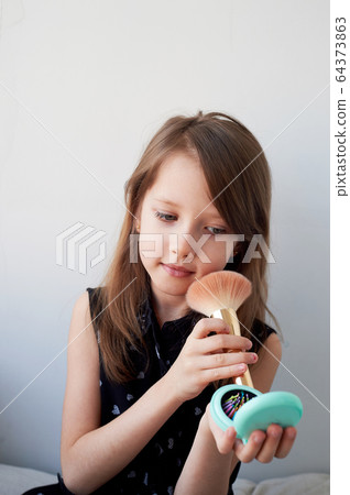 The girl is 6 years old on a light background, powders her cheeks with a brush.Striving for beauty, mother's cosmetics. The girl is 6 years old on a light background, powders her cheeks with a brush.Striving for beauty, mother's cosmetics. 64373863