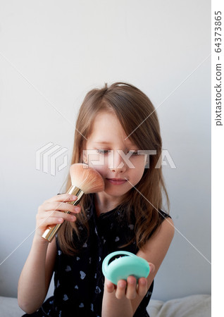 The girl is 6 years old on a light background, powders her cheeks with a brush.Striving for beauty, mother's cosmetics. The girl is 6 years old on a light background, powders her cheeks with a brush.Striving for beauty, mother's cosmetics. 64373865