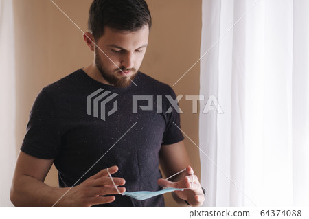 Man put on madical mask at home. Young man in protective mask. Coronavirus theme Man put on madical mask at home. Young man in protective mask. Coronavirus theme 64374088
