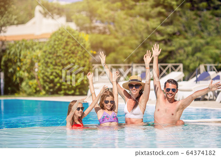 Happy family of four in outdoors swimming pool 64374182