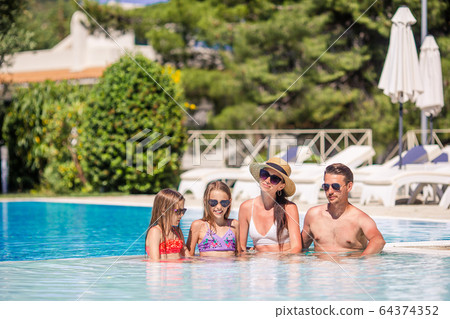 Happy family of four in outdoors swimming pool 64374352