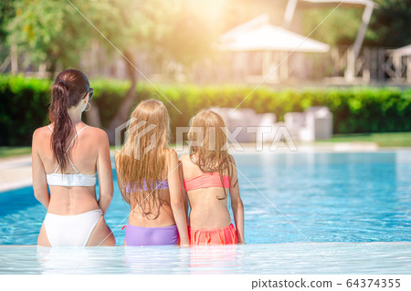 Mother and two kids enjoying summer vacation in luxury swimming pool Mother and two kids enjoying summer vacation in luxury swimming pool 64374355