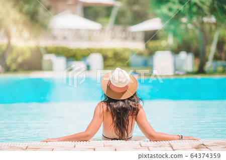 Young beautiful woman enjoying summer vacation in luxury swimming pool 64374359