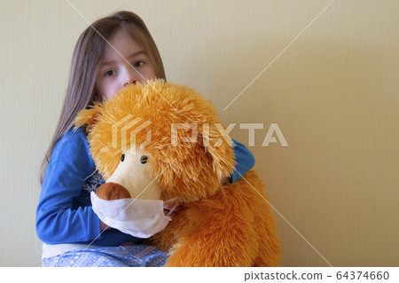 A little girl holds a teddy bear in a mask for protection during quarantine. Pandemic Protection Concept.copyspace for text. 64374660