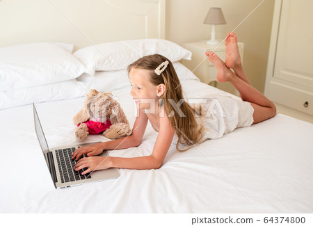 Serious schoolgirl sitting at table with laptop and textbook and doing homework. Serious schoolgirl sitting at table with laptop and textbook and doing homework. 64374800