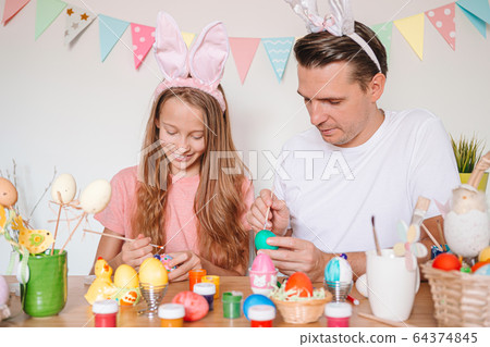 Father and his little daughter painting eggs. Happy family preparing for Easter. 64374845