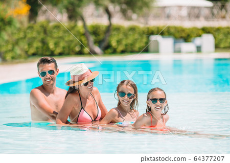 Happy family of four in outdoors swimming pool 64377207