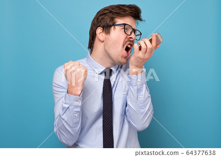 Angry businessman in shirt and tie holding mobile 64377638