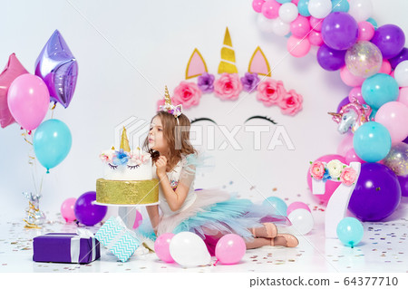 Unicorn Girl posing near happy birthday cake. Idea for decorating unicorn style birthday party. Unicorn decoration for festival party girl 64377710