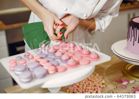 Confectioner in a uniform decorates the macaroni Confectioner in a uniform decorates the macaroni 64378063