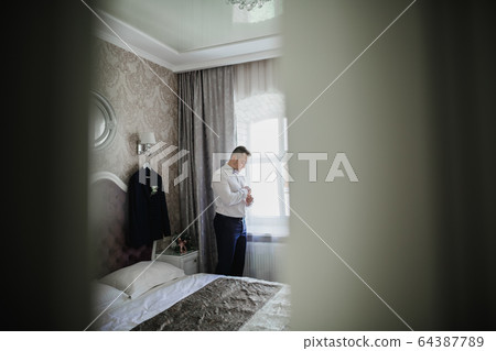 Grooms morning preparation. Handsome man getting dressed and preparing for the wedding 64387789