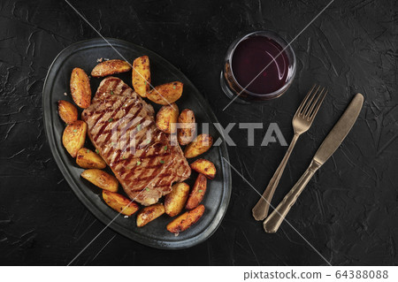Grilled beef steak with baked potato wedges, with a glass of wine, shot from the top on a black background Grilled beef steak with baked potato wedges, with a glass of wine, shot from the top on a black background 64388088
