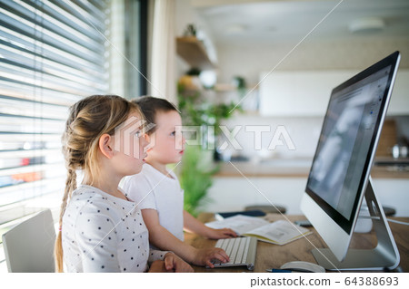 Small girl and boy using computer indoors at home. Corona virus and quarantine concept. Small girl and boy using computer indoors at home. Corona virus and quarantine concept. 64388693