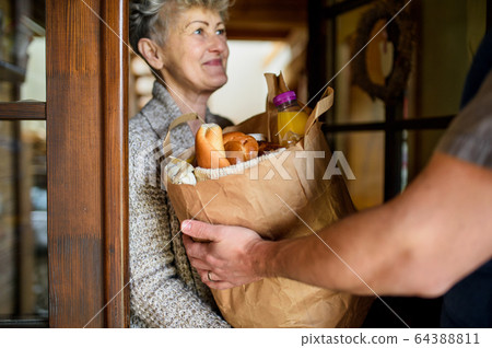 Unrecognizable courier delivering shopping to senior woman. 64388811