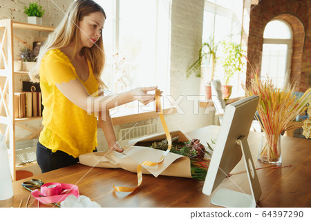 Florist at work: woman shows how to make bouquet, working at home concept, using paper coverage Florist at work: woman shows how to make bouquet, working at home concept, using paper coverage 64397290