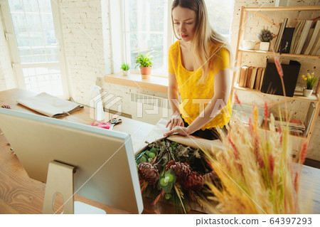 Florist at work: woman shows how to make bouquet, working at home concept, using paper coverage Florist at work: woman shows how to make bouquet, working at home concept, using paper coverage 64397293
