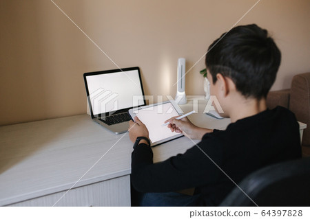 Handsome young boy drawing on tablet at home. Teenage boy use tablet for work. Schoolboy study at home using tablet, laptop, smartphone Handsome young boy drawing on tablet at home. Teenage boy use tablet for work. Schoolboy study at home using tablet, laptop, smartphone 64397828