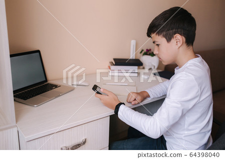 Schoolboy study at desk in his room. Boy use laptop and smartphone to writing in notebook. Books and tablet on the table. Study home during qurantine. Mock up Schoolboy study at desk in his room. Boy use laptop and smartphone to writing in notebook. Books and tablet on the table. Study home during qurantine. Mock up 64398040