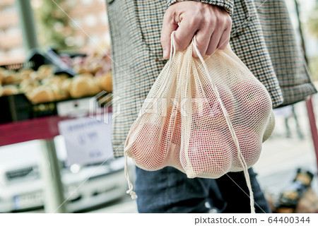 man using a reusable mesh bag at a greengrocer 64400344