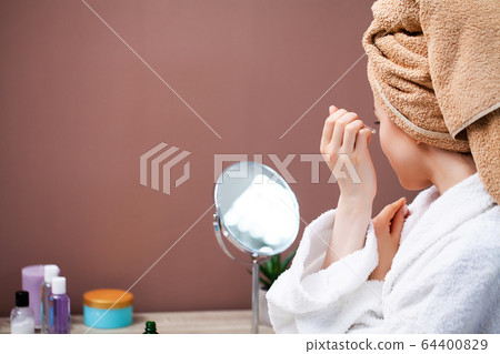 Pretty girl doing cosmetic procedures at home in front of mirror. 64400829