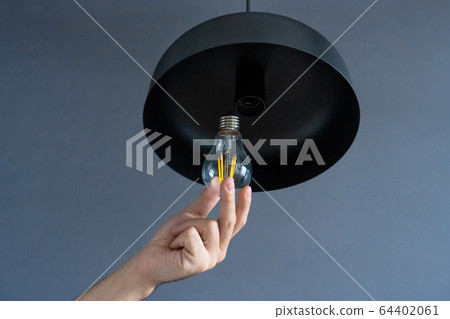 Close-up. A hand changes a light bulb in a stylish Close-up. A hand changes a light bulb in a stylish 64402061