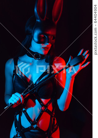 sexy girl mistress in leather harness and Bunny mask holds a Flogger whip 64404904