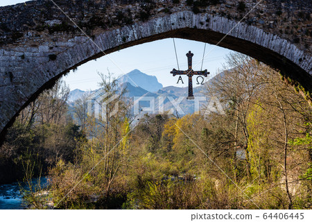 Cross hanging from old Roman stone bridge with mountains on background 64406445