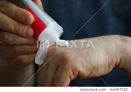 Male hands applying moistening cream from little tube on skin 64407885