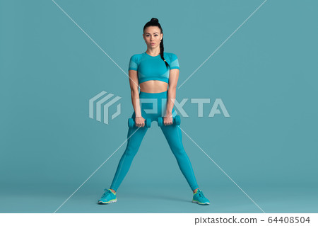 Beautiful young female athlete practicing on blue studio background, monochrome portrait 64408504