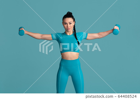 Beautiful young female athlete practicing on blue studio background, monochrome portrait Beautiful young female athlete practicing on blue studio background, monochrome portrait 64408524