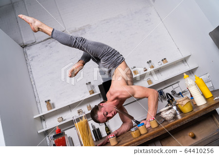 Muscular man stand on one the hand in the kitchen and holding knife. Concept of healthy lifestyle and organic food Muscular man stand on one the hand in the kitchen and holding knife. Concept of healthy lifestyle and organic food 64410256