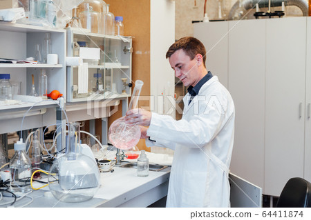 male scientist conducts chemical experiments with liquids in science lab male scientist conducts chemical experiments with liquids in science lab 64411874