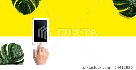 Person using a tablet computer with tropical leaves Person using a tablet computer with tropical leaves 64411920