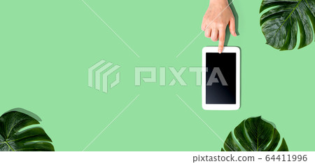 Person using a tablet computer with tropical leaves Person using a tablet computer with tropical leaves 64411996