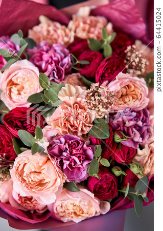 Bright berry color, Beautiful bouquet of mixed flowers in womans hands. the work of the florist at a flower shop. Delivery fresh cut flower. European floral shop. 64415024