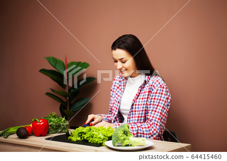 Pretty woman preparing a dietary salad of fresh vegetables at home in the kitchen Pretty woman preparing a dietary salad of fresh vegetables at home in the kitchen 64415460