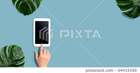 Person using a tablet computer with tropical leaves Person using a tablet computer with tropical leaves 64418390