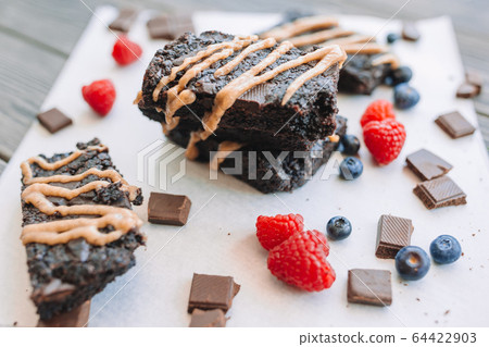 Chocolate nut brownie cake in female hands decorated with strawberries and blueberry Chocolate nut brownie cake in female hands decorated with strawberries and blueberry 64422903