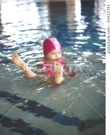 little girl in a pool cap and pink swimsuit learns to swim in the pool little girl in a pool cap and pink swimsuit learns to swim in the pool 64423343