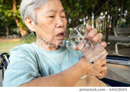 Asian senior woman holding glass of water,hands shaking while drinking water,elderly with hands tremor uncontrolled body tremors,symptom of essential tremor,parkinson's disease,neurological disorders 64429004