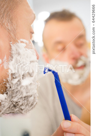 Guy shaving his beard in bathroom Guy shaving his beard in bathroom 64429666