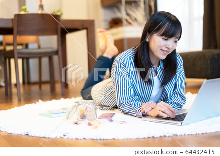 Young woman looking at smartphone while lying in the living room Young woman looking at smartphone while lying in the living room 64432415