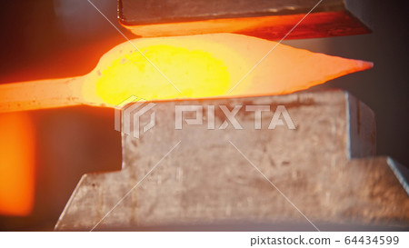 Blacksmith making a knife out of hot metal using a pressure machine 64434599