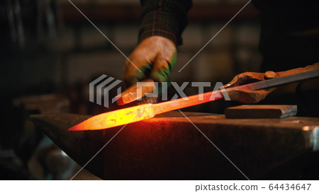 Forging industry - blacksmith brushing off the shavings of piece of hot metal 64434647