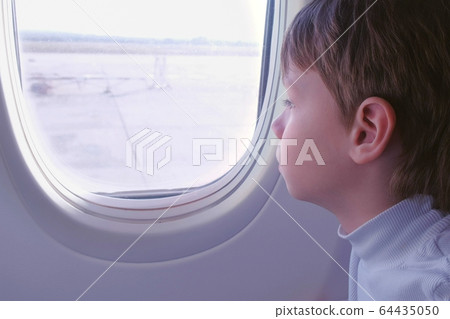 Boy looks out the window when the plane takes off. Side view. 64435050