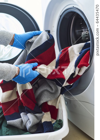 man putting clothes into the washing machine 64435470