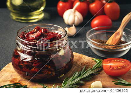 Cooking sun-dried tomatoes in a glass jar with olive oil, garlic and rosemary 64436335