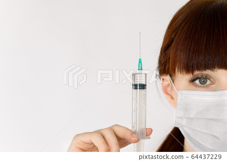 Close-up of half face female doctor portrait, wearing sterile medical mask, holding syringe with vaccine or drug, on white background with copyspace advertising area. Stop deseases, covid-19 Close-up of half face female doctor portrait, wearing sterile medical mask, holding syringe with vaccine or drug, on white background with copyspace advertising area. Stop deseases, covid-19 64437229