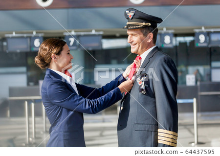 Young attractive flight attendant adjusting pilot 64437595