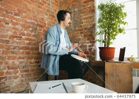 Caucasian musician playing hand drum during online concert at home isolated and quarantined, improvising 64437975